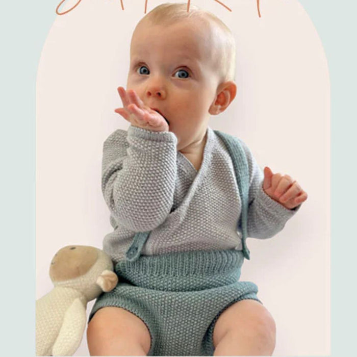 Baby wearing knitted romper and jacket set from CRU2319 pattern, using CRUCCI Luxury Merino Crepe 4ply.