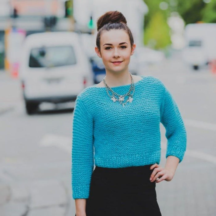 Cropped blue sweater knitting pattern, worn outdoors, designed for 12-ply yarn.
