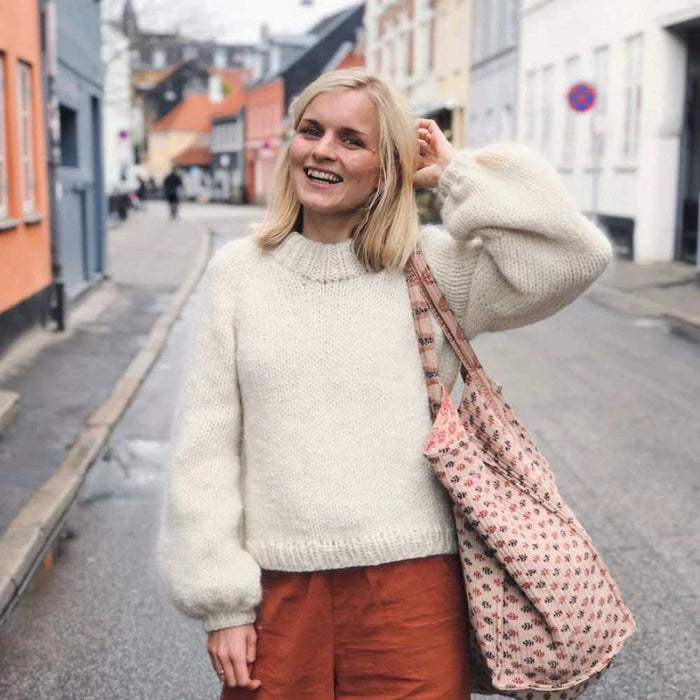 Woman wearing white knitted sweater in urban street, showcasing Petite Knits holiday sweater pattern.