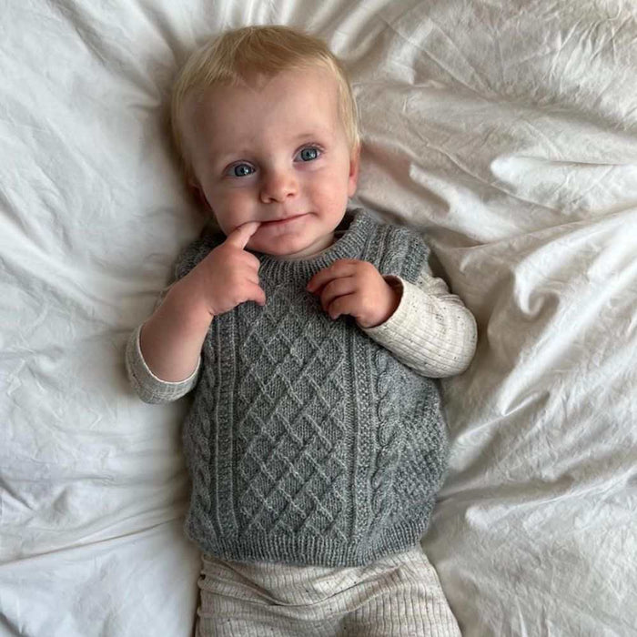 Baby wearing a gray cable-knit slipover, lying on a white blanket.