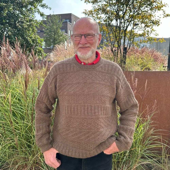 Man wearing Storm Sweater knit from PetiteKnit pattern, textured design, outdoors.