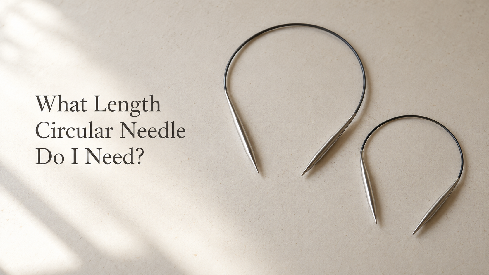 Two circular knitting needles of different lengths on a neutral background.