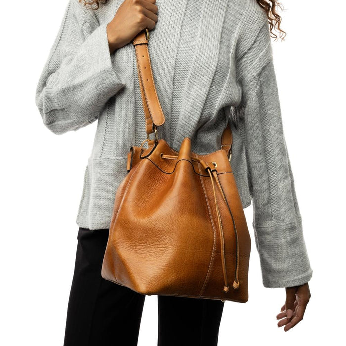 Genuine leather bucket bag in burned tan and gold with adjustable strap and drawstring, perfect for knitting projects.