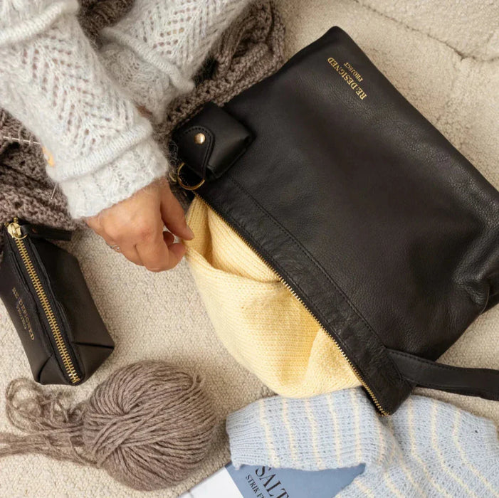 Knitting bag in black and gold leather with yarn and accessories inside.