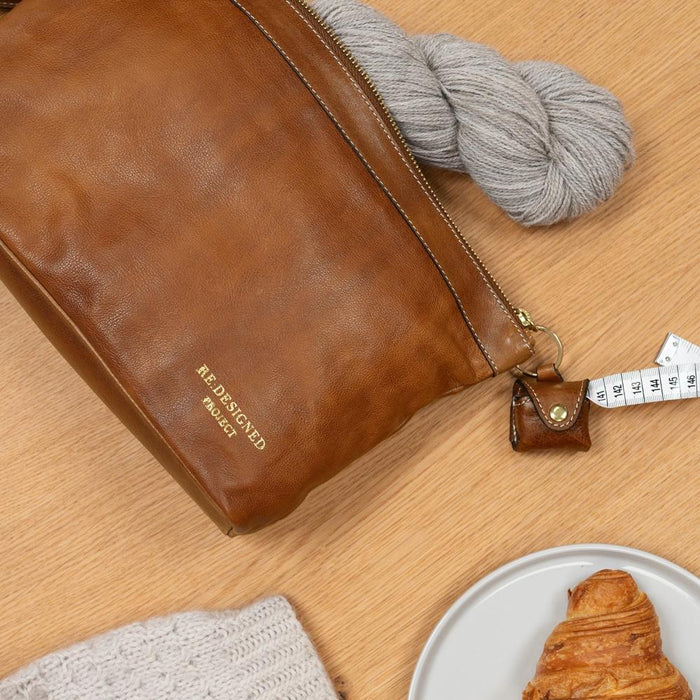 Knitting bag in soft burnt tan leather with metal zipper and side handle, featuring open pockets and keyring for accessories.