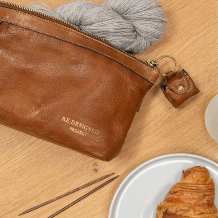 Burned tan and gold leather knitting bag with metal zipper, open pockets, and side handle.
