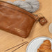 Burned tan and gold leather knitting bag with metal zipper, open pockets, and side handle.