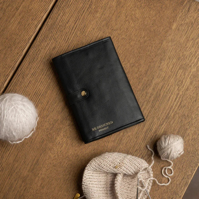 Black and gold leather knitting bag for circular needles on wooden table.
