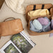 Taupe leather knitting project bag with yarn and organized compartments.