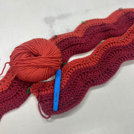Crocheted red temperature blanket in progress with yarn ball and hook.