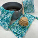 Blue, white and green Waves knitted washcloths beside a bowl and wooden dish brush