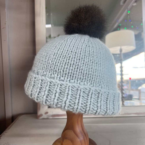 Pale blue knitted beanie with a folded ribbed brim and dark fur pom pom
