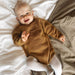 Baby wearing Anker's Suit knitted romper in brown, PetiteKnit pattern for infants 1-24 months.