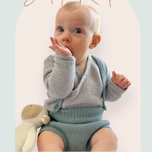 Baby wearing knitted romper and jacket set from CRU2319 pattern, using CRUCCI Luxury Merino Crepe 4ply.