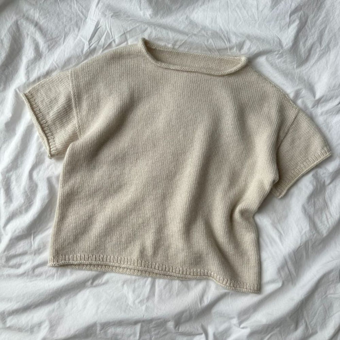 Cloud Tee Knitting Pattern by PetiteKnit displayed on a light fabric background, showcasing simple creamy knit design with short sleeves and a round neck.