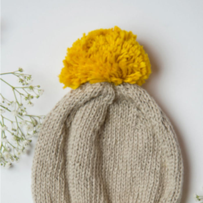 Knitted Sol Hat pattern with ribbed brim and yellow pom-pom, ideal for cold weather.