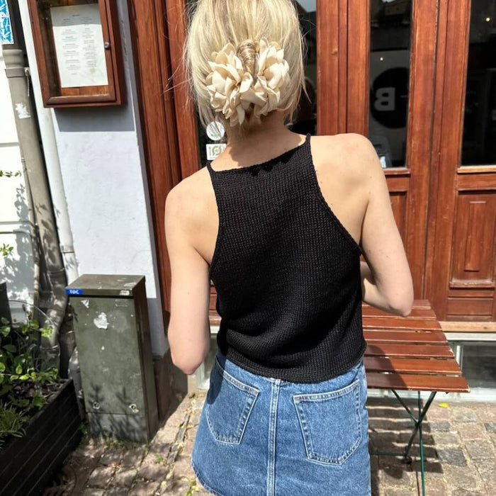 Woman wearing hand-knitted black top with i-cord straps, styled with a denim skirt, back view.