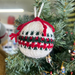 Knitted Christmas bauble on tree with red, white, and green pattern.