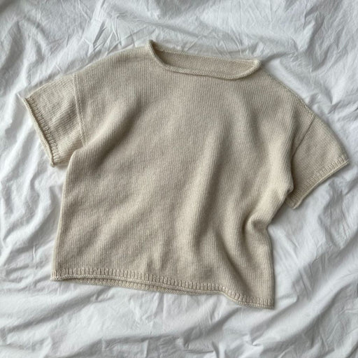 Cloud Tee Knitting Pattern by PetiteKnit displayed on a light fabric background, showcasing simple creamy knit design with short sleeves and a round neck.