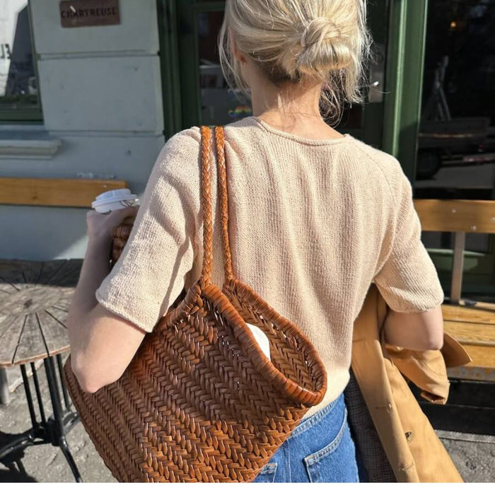 Woman wearing a Cumulus Tee O-neck in stockinette stitch with i-cord edges, holding a wicker bag, showcasing the knitting pattern by PetiteKnit.