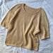 Cumulus Tee O-neck knitting pattern by PetiteKnit laid on fabric background.
