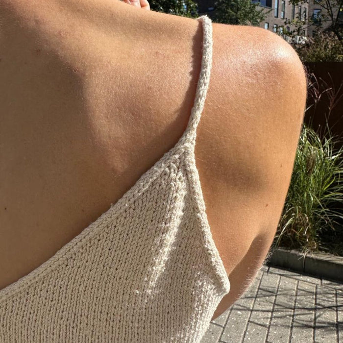 Close-up of a back view of a hand-knitted top with thin straps and a V-neck design in natural light, showcasing the PetiteKnit Cumulus Top texture.