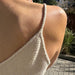 Close-up of a back view of a hand-knitted top with thin straps and a V-neck design in natural light, showcasing the PetiteKnit Cumulus Top texture.