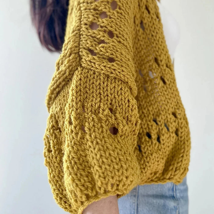 Yellow eyelet cardigan on woman in jeans, showcasing knitted texture and three-quarter sleeves.