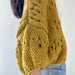 Yellow eyelet cardigan on woman in jeans, showcasing knitted texture and three-quarter sleeves.