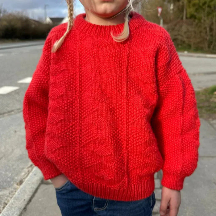 Child wearing red textured knit sweater from PetiteKnit Esther Sweater Junior knitting pattern.