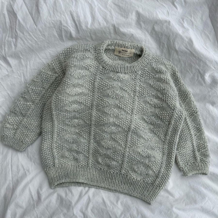 Esther Sweater Junior knitting pattern, textured design on flat surface.