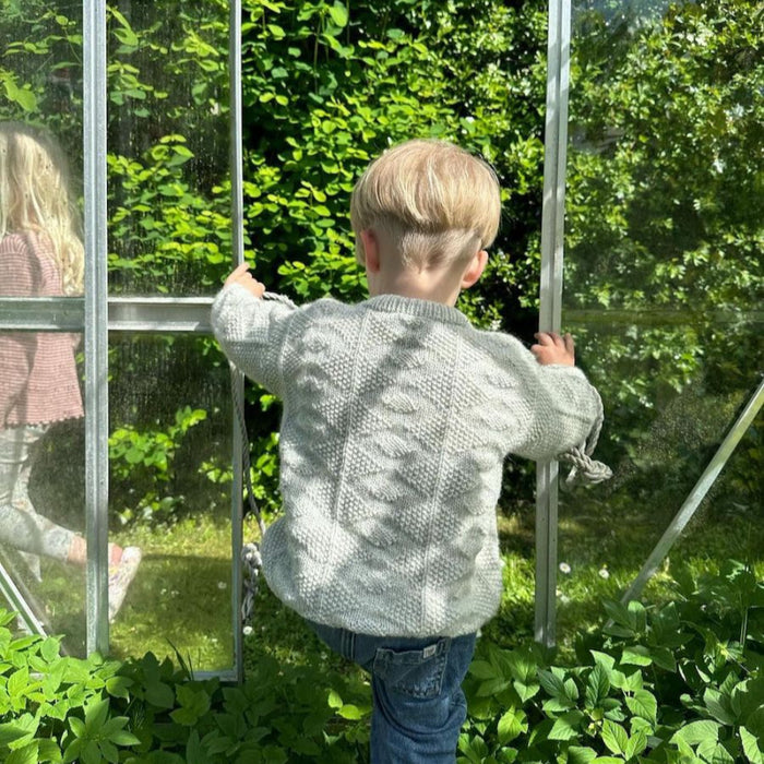 Child wearing a textured white knitted sweater in a garden setting.