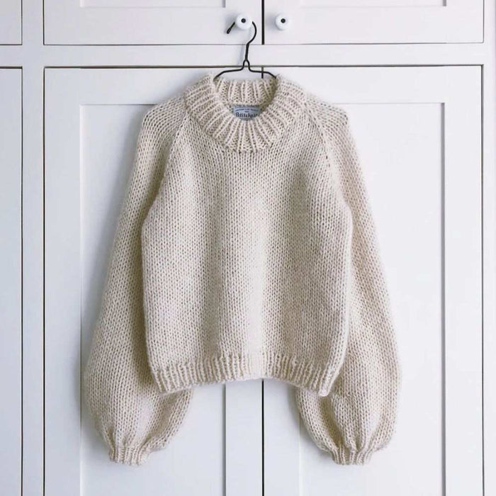 Holiday sweater knitting pattern by PetiteKnit, featuring cozy oversized style with ribbed cuffs and hem in cream color.