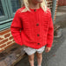 Child wearing a hand-knitted red Esther Jacket by PetiteKnit with button closure and textured design.