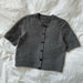 PetiteKnit Maggie Cardigan knitting pattern showcasing a short-sleeve, button-up design in gray.