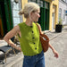 Maggie Vest knitted from PetiteKnit pattern, vibrant green with black buttons, styled casually outdoors.