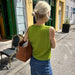 Woman wearing a green Maggie Vest and carrying a woven bag; PetiteKnit knitting pattern.