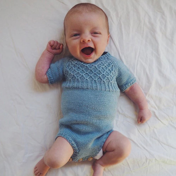 Baby wearing blue knitted summer suit by PetiteKnit with smocking stitch yoke.
