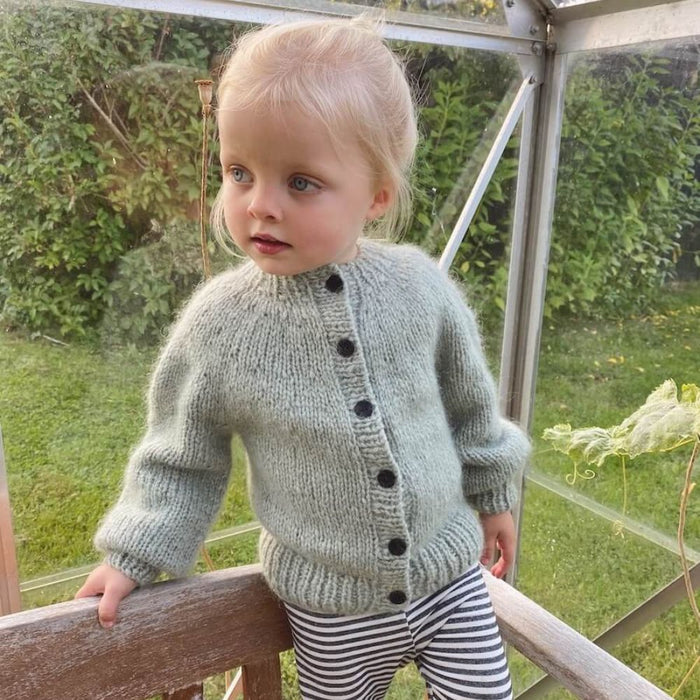 Child wearing a PetiteKnit Novice Cardigan Mini Chunky Edition, hand-knitted from soft yarn with button closure and ribbed edges.