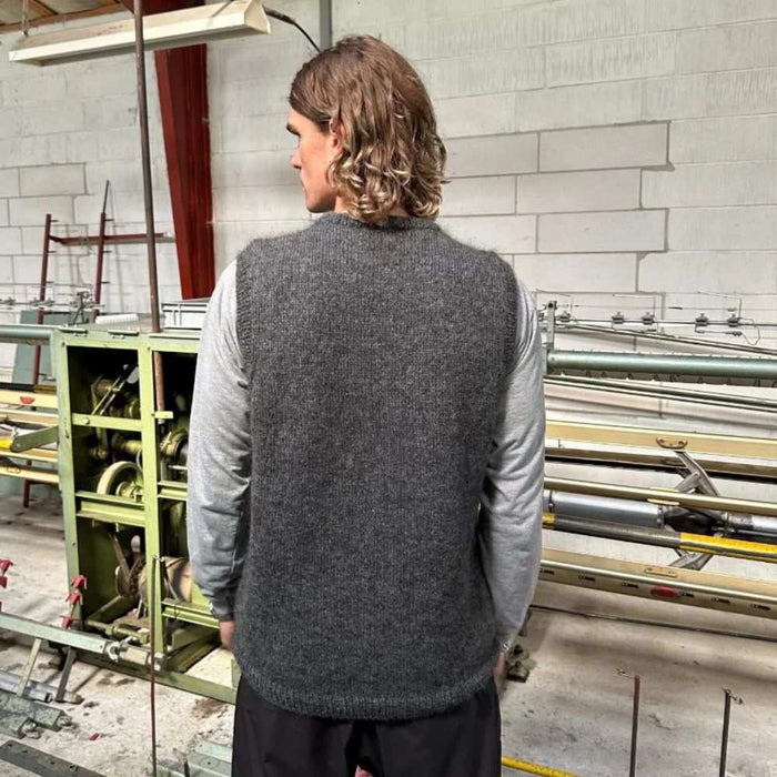 Man wearing dark gray knitted slipover, back view, in industrial setting; Petite knits pattern display.