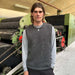 Man wearing a gray knitted slipover in an industrial setting, PetiteKnit pattern.