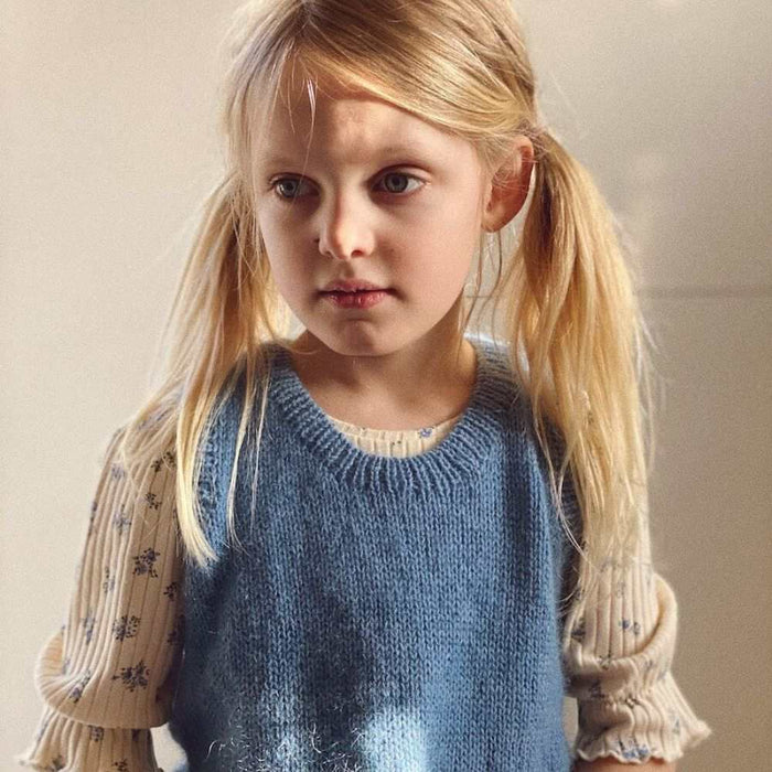 Child wearing a blue Stockholm Slipover Mini, PetiteKnit design with ribbed edges.
