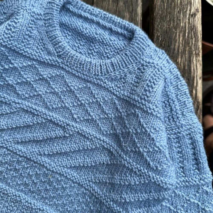 Blue knitted baby sweater with textured pattern, part of the Storm Sweater Baby knitting pattern by PetiteKnit.