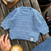 Baby blue textured knit sweater on wooden table, PetiteKnit pattern.