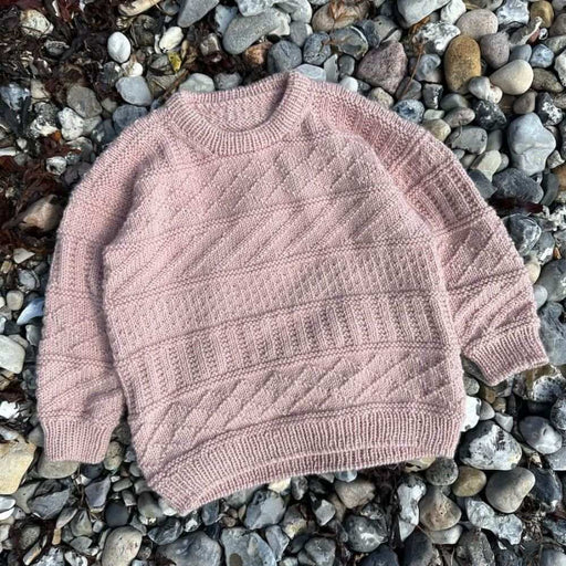Pink textured Storm Sweater Junior on pebbles; PetiteKnit knitting pattern.