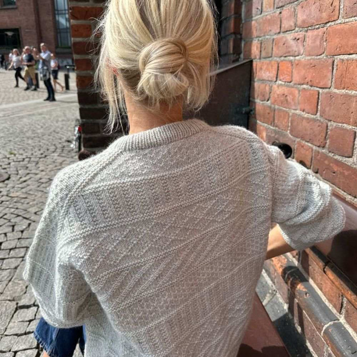 Back view of a woman wearing a Storm Sweater in a textured knitting pattern, showcasing the detailed yoke and ribbed neck edge, by PetiteKnit.