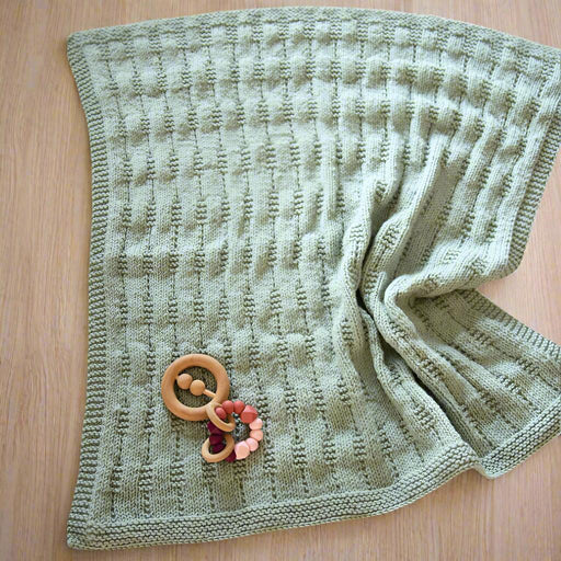 Textured baby pram blanket with garter stitch border, knitted in New Zealand Merino 12ply yarn, displayed on a wooden surface.