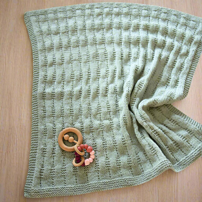 Textured baby pram blanket with garter stitch border, knitted in New Zealand Merino 12ply yarn, displayed on a wooden surface.