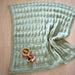 Textured baby pram blanket with garter stitch border, knitted in New Zealand Merino 12ply yarn, displayed on a wooden surface.