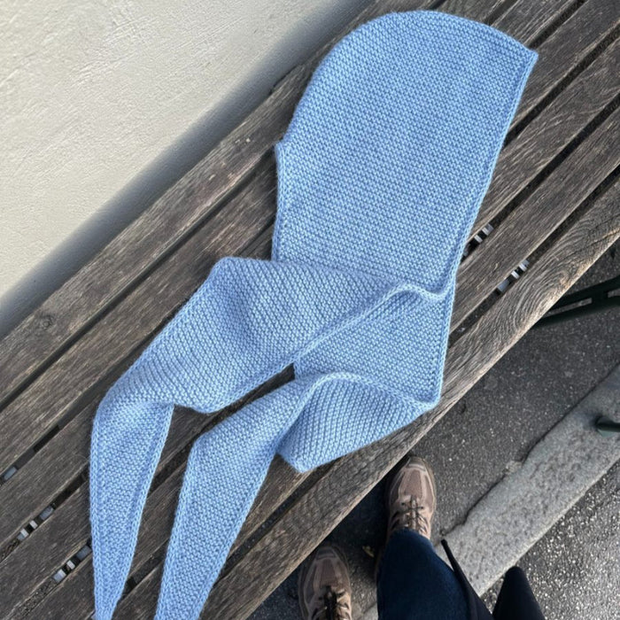 Cozy blue knitted hooded scarf on wooden bench; Sophie Hood knitting pattern.